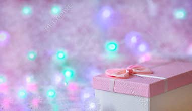 A gift box of soft pink color on a defocused background with burning lights of a garland. Festive, Christmas background. Free
