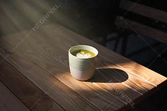 A cup of green tea matcha latte on wooden table at cafe. Healthy food concept. Sun rays. Side view. Close-up