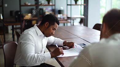 African American business man studying paper document and signing contract sitting at office desk.