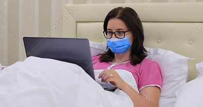 Woman with medical mask working from home on laptop computer during the pandemic