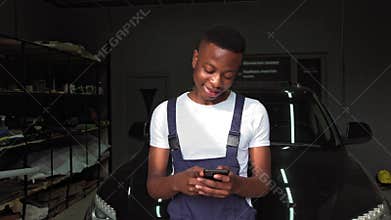 Portrait of handsome african american man standing in center of camera having cellphone in hands. He looks happy and