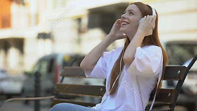 Pleased redhead teen listening to music, taking headset off and smiling to cam