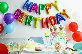 Table with treats and phrase HAPPY BIRTHDAY  of colorful balloon letters in living room