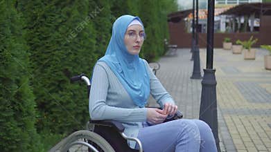 Portrait lonely sad young muslim woman disabled in a traditional scarf sitting in a wheelchair in the park