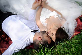 Happy wedding couple lying on green grass at the summer time