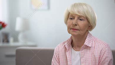 Upset elderly woman sitting alone in nursing home, abandoned by relatives