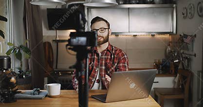 Happy young successful Caucasian professional blogger man smiles making video for vlog using camera at home slow motion.