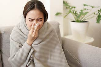 Asian Cute of  girl having  flu season  and  sneeze  using paper tissues sitting on sofa at home, Putting blanket, Health and
