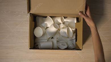 Lady hands putting disposable cups in cardboard box with word Cellulose written
