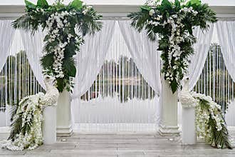 Luxury wedding arch decorated with palm leaves, orchid flowers and floral peacocks outdoors, copy space. Wedding ceremony.