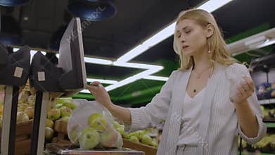 Middle-aged woman weighs a bag of apples in the supermarket.