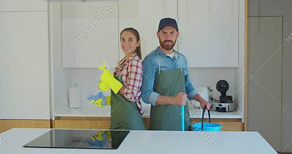 Portrait of a couple as a professional cleaners in uniform standing together with cleaning tools indoors.