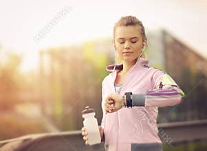 Woman running at sunset in city park using smart watch and earbuds
