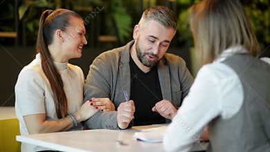 Side view of realtor and young couple sitting at office desk discussing property for sale. Happy couple became a house