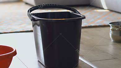 Water pouring into bucket, bowl and pot standing on living room floor, flooding