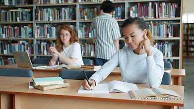Group of students working in library reading books writing studying indoors