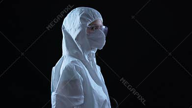 Lab worker in protective suit and mask turning to camera against dark background