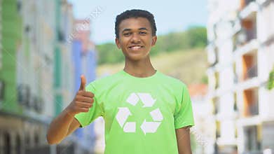 Joyous mixed-race teen in recycling symbol t-shirt gesturing thumbs-up, ecology