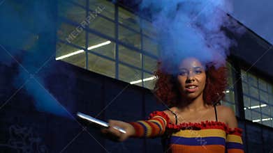 Attractive mixed-race girl clubbing in cloud of blue smoke, self-expression