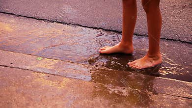 Feet of a barefoot child stand in a puddle during golden hour as gentle raindrops fall