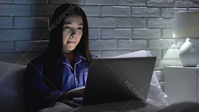 Woman lying in bed working hastily on laptop, trying to meet deadline, overhours