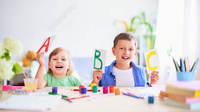 A little girl and a boy learn at home. happy kids at the table with school supplies smiling funny and learning the alphabet in a