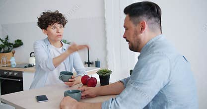 Unhappy couple man and woman agruing sitting at table in kitchen talking