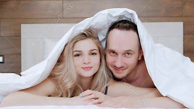 A young married couple, a man and a woman are lying on a bed with white linens. Morning and awakening.