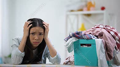 Frustrated housewife looking at laundry basket full of clothes, overworking