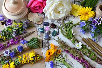 Top view of witchery scrolls with magic herbs, summer flowers and crystals on table