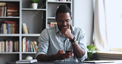 Happy young adult African man using smartphone in home office