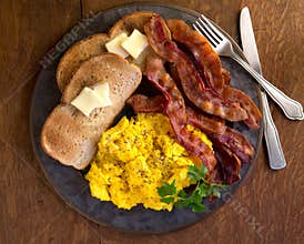 Srambled eggs, bacon and toast plated on a wood table