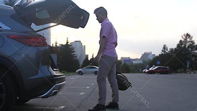 Young handsome man opens trunk put backpack and close it. Automatic system opening the trunk by leg. slow motion