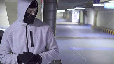Thief in a balaclava is waiting for the victim in the parking car