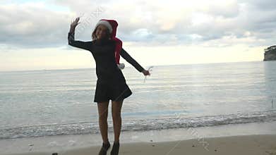 Funny woman in Santa hat jumping near the sea