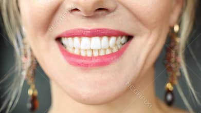 Extreme close-up female mouth with pink lipstick smiling showing white healthy beautiful teeth