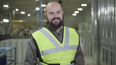 Portrait of bald Caucasian man with beard standing at warehouse, looking at camera and smiling. Happy worker at his