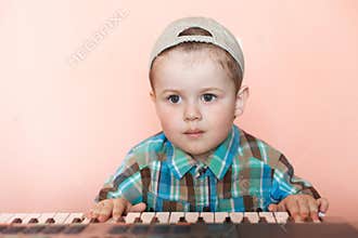 Portrait of a pretty boy wearing baseball cap backwards playing the digital piano