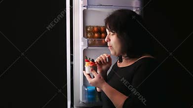 Woman night at the fridge eating a cake.Hunger,overeating,diet.