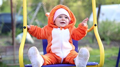 Happy little baby infant swinging on a swing. The girl is dressed in a cosplay fox costume. Pajamas called kigurumi.