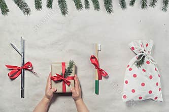 Zero waste plastic free christmas gift flatlay. Child`s hands holding gift box in craft paper wrapping, reusable metal straws,