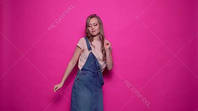 Funny young woman is dancing and having fun on isolated pink background.