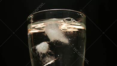 Close-up of hand throwing ice cubes into a glass with water, isolated on black background.