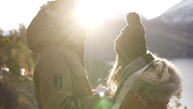 Young couple standing embrace kissing, looking landscape sunny winter day. Woman and man in warm clothes standing in
