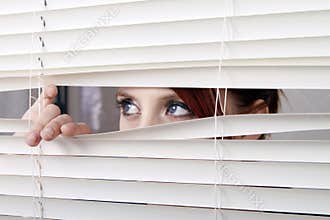 Woman looking through window blinds