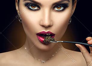 Beautiful Fashion Model woman eating black caviar. Beauty girl portrait with caviar on her lips. Female with spoon of black Caviar