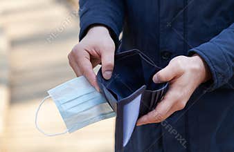 Man holds a medical mask and empty wallet without money. Bankruptcy and unemployment resulting from the global coronavirus