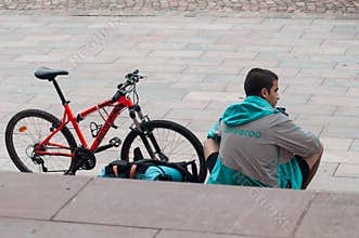 Delivery man from deliveroo british company  in mountain bike waiting for  delivery to be made sitting on stairs in outdoor