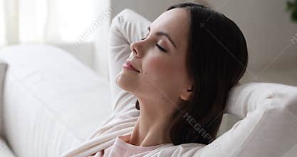 Serene young woman relaxing on sofa breathing air, close up