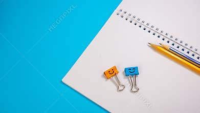 Notepad with Pencils and Orange and Blue Binder Clip on Blue Background